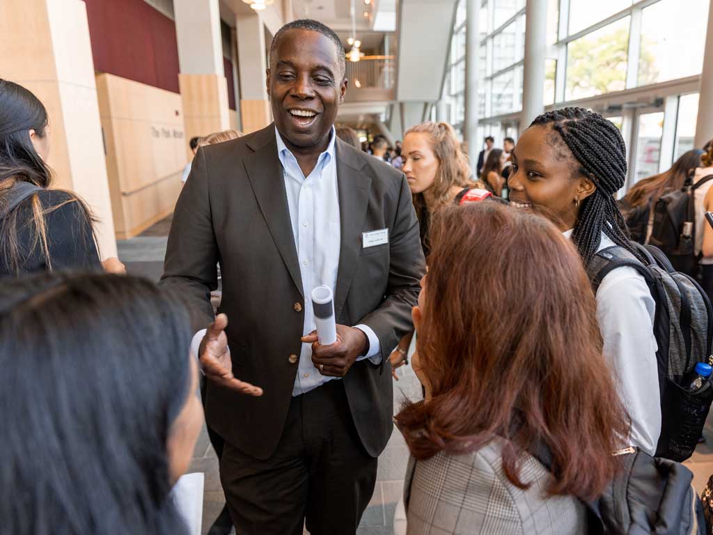 An alum speaks with a semi-circle of students around them.