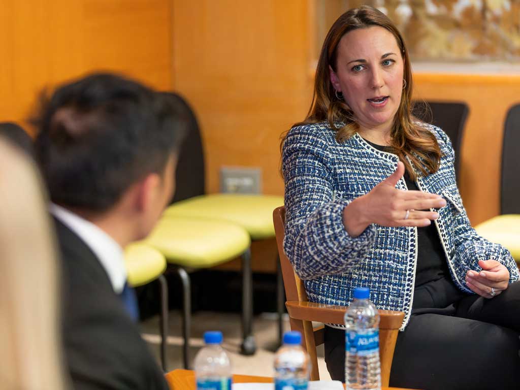 A woman speaks and gestures to a person in the foreground.