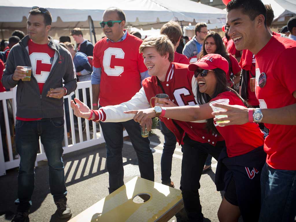 People in Cornell attire play cornhole outside.