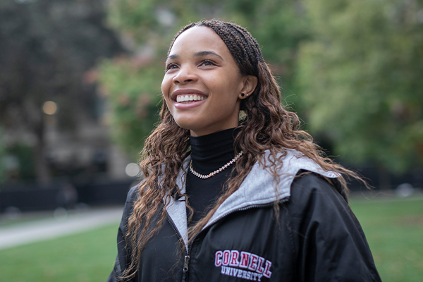 A woman in a Cornell University windbreaker jacket stands outside.