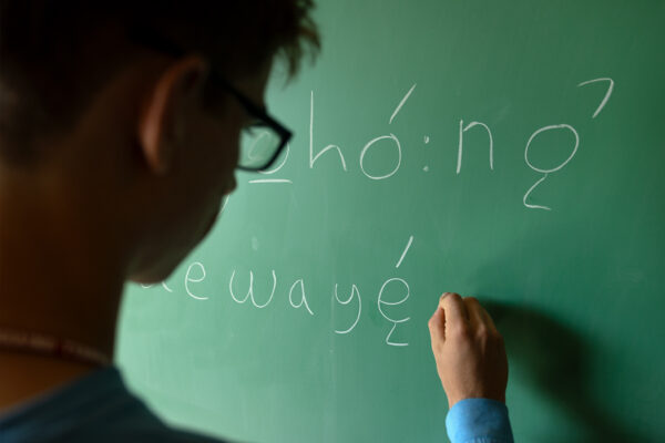 Student writes with walk chalk on a green chalkboard.
