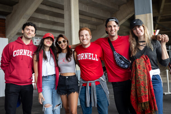 Students wear red Cornell gear and stand together smiling.