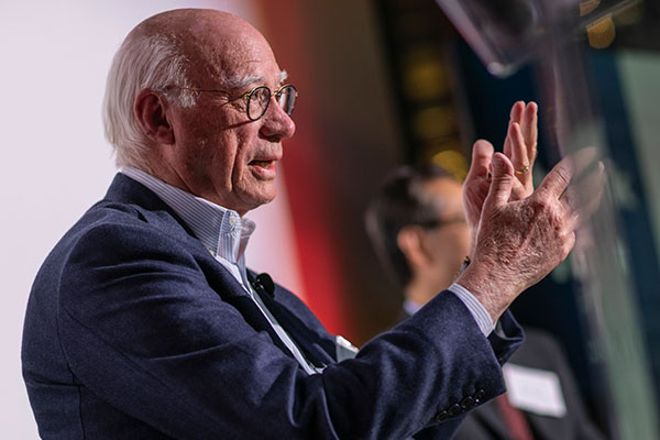 A close-up photo of a man’s head and hands as he gestures with his hands and speaks.