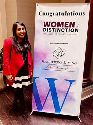 Deepilka Cattry standing next to a Women of Disctinction banner.