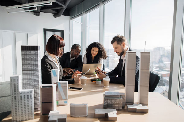 Hospitality professionals sitting around a conference table with architectural building models, discussing a project in a modern office.