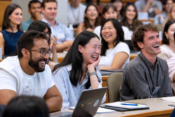 MBA students laughing and engaged during a classroom discussion in a tiered lecture hall.