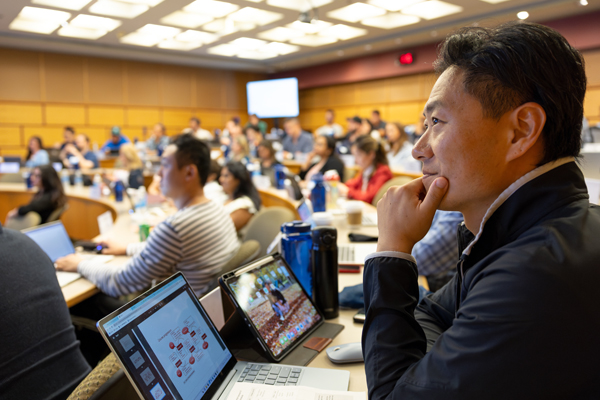 H1-B student sitting in a large university lecture hall with a laptop open in front of them